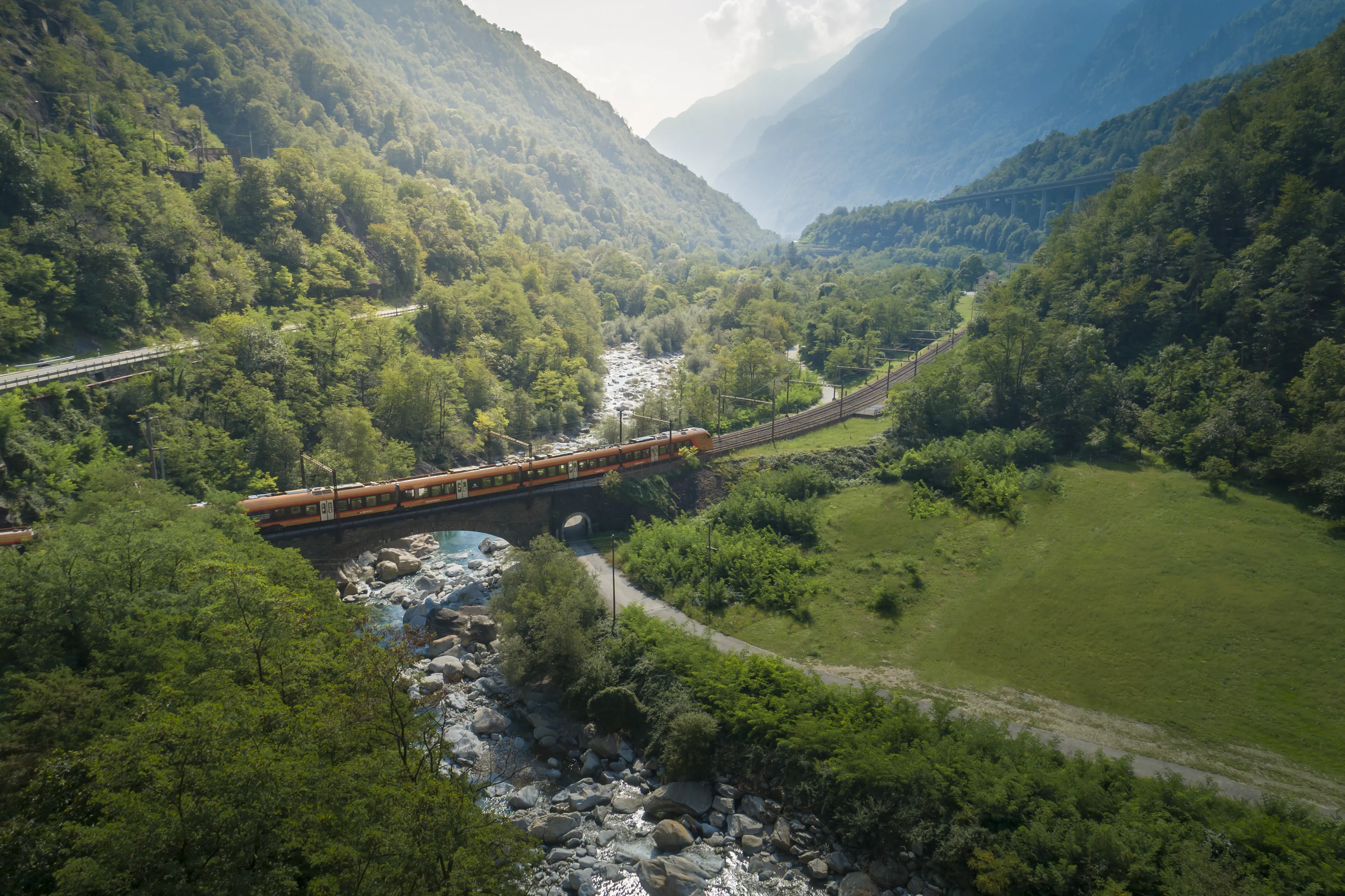 Près de Wassen, le Treno Gottardo traverse un paysage verdoyant et passe sur un pont qui enjambe une rivière.