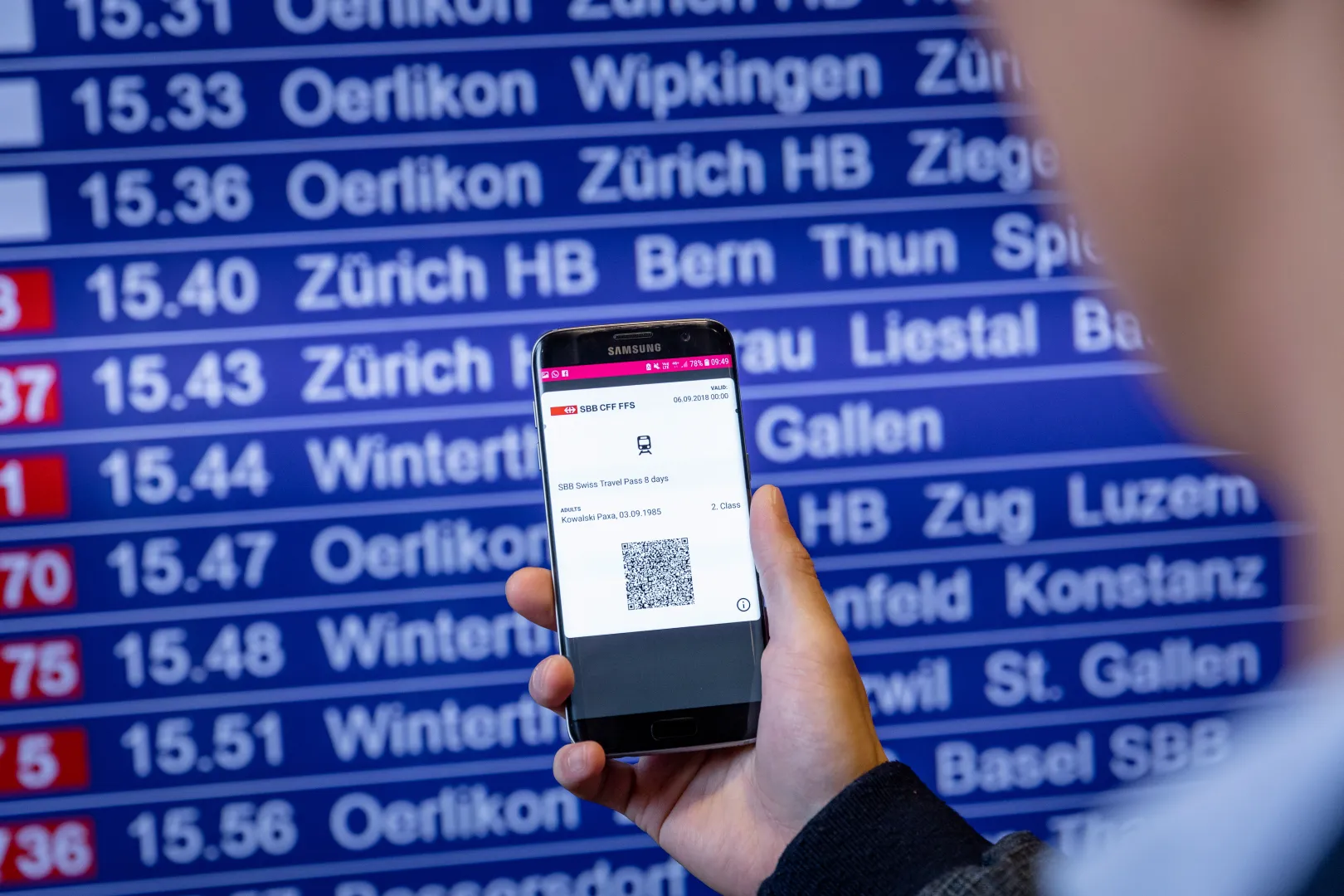 Le Swiss Travel Pass est affiché sur un smartphone, au premier plan le tableau des horaires.